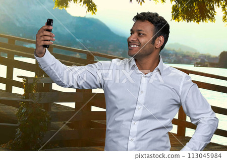 Smiling indian businessman taking selfie on his phone outdoors. People, technology and tourism concept. 113045984