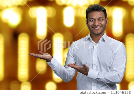 Handsome businessman looking at camera while presenting something on golden bokeh background. Winter holiday special offer. 113046138