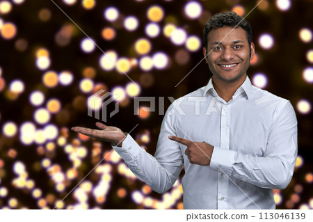 Handsome man looking at camera while presenting something on festive bokeh background. Christmas holiday deal. Handsome man looking at camera while presenting something on festive bokeh background. Christmas holiday deal. 113046139