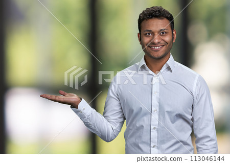 Successful young businessman showing empty space on blurred background. Man showing copy space on blur bokeh background. 113046144