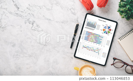 Tablet with a pen on it and a cup of coffee next to it. The tablet has a lot of graphs and numbers on it 113046853