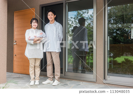 Owner couple and baby standing in front of the entrance of a newly built home/detached house/detached house/couple/family Owner couple and baby standing in front of the entrance of a newly built home/detached house/detached house/couple/family 113048035