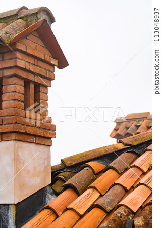 Fragment of old weathered ceramic red tile roof, chimney on the building 113048937