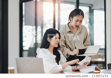 Two professional women share a cheerful moment while collaborating on a project in a bright and modern office environment. 113051215