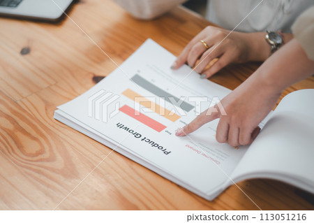 Close up of a professional hands pointing at a growth chart while analyzing business performance in a detailed report. Close up of a professional hands pointing at a growth chart while analyzing business performance in a detailed report. 113051216