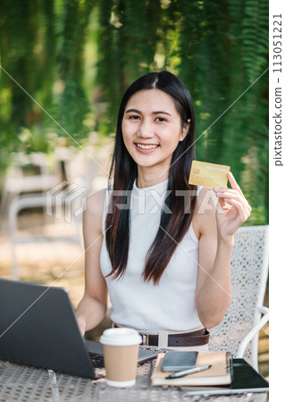 Young woman looking at camera holding credit card and using laptop computer on desk. Online shopping concept 113051221