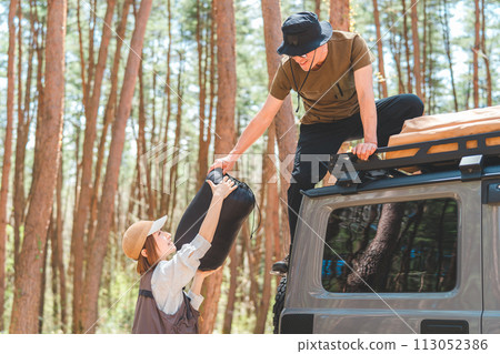 A man and a woman, a married couple, a couple loading and unloading luggage from a roof rack of a car at an auto camping site A man and a woman, a married couple, a couple loading and unloading luggage from a roof rack of a car at an auto camping site 113052386
