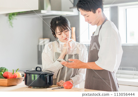 A couple cooking in the kitchen while looking at their smartphones (recipe site/recipe app) A couple cooking in the kitchen while looking at their smartphones (recipe site/recipe app) 113056444