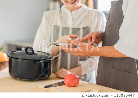 A couple cooking in the kitchen while looking at their smartphones (recipe site/recipe app) 113056447