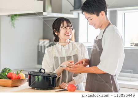 A couple cooking in the kitchen while looking at their smartphones (recipe site/recipe app) A couple cooking in the kitchen while looking at their smartphones (recipe site/recipe app) 113056449