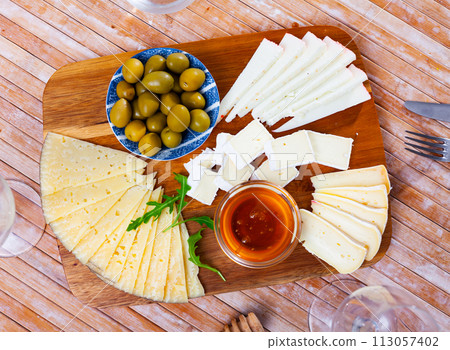 On wooden table there is cutting board with assorted cheese, honey, pickled olives - On wooden table there is cutting board with assorted cheese, honey, pickled olives - 113057402
