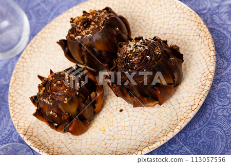 Popular Spanish vegetarian appetizer of broiled artichokes on plate 113057556