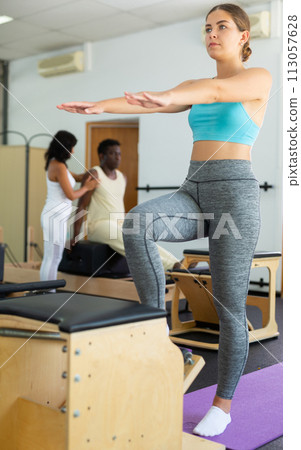 Girl performing set of pilates exercises on reformer in modern fitness studio 113057628