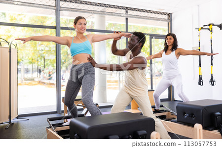 Female pilates trainer helping pilates people during training Female pilates trainer helping pilates people during training 113057753