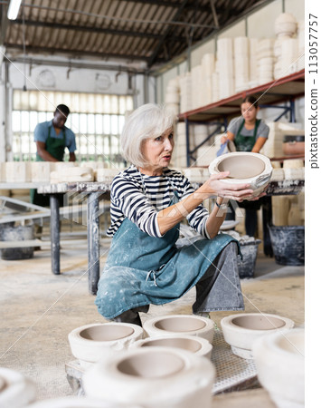 Elderly worker demonstrates half of plaster mold for pottery. 113057757