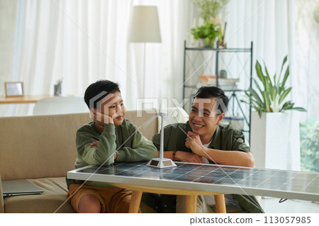 Dreamy father and son looking at small model of wind turbine with rotating blades Dreamy father and son looking at small model of wind turbine with rotating blades 113057985