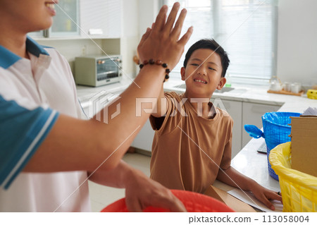 Happy kid giving father high five after sorting garbage at home 113058004