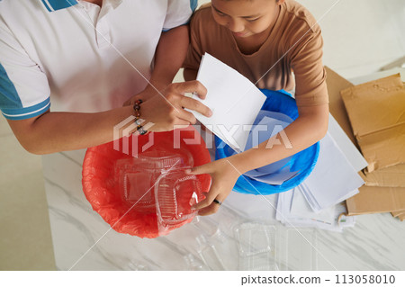 Father teaching son to sort waste at home, separating paper and plastic, view from above 113058010