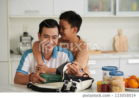 Happy son hugging father packing his lunch bag Happy son hugging father packing his lunch bag 113058014