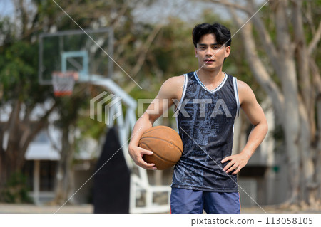 Portrait of man in activewear holding a ball standing on the basketball court 113058105