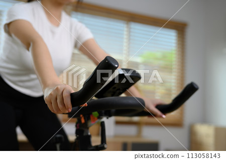 Cropped shot of young woman doing cardio on stationary bike at home Cropped shot of young woman doing cardio on stationary bike at home 113058143