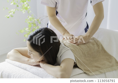 Young woman having her shoulders massaged Young woman having her shoulders massaged 113058791