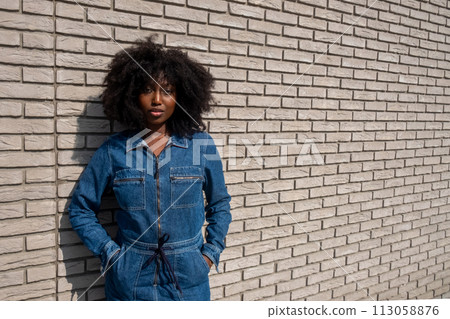 Confident Young Woman in Chic Denim Outfit Against Brick Wall Confident Young Woman in Chic Denim Outfit Against Brick Wall 113058876