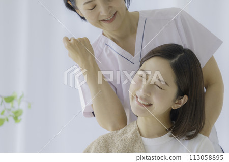 一位面容痛苦的年輕女子接受肩膀按摩 113058895