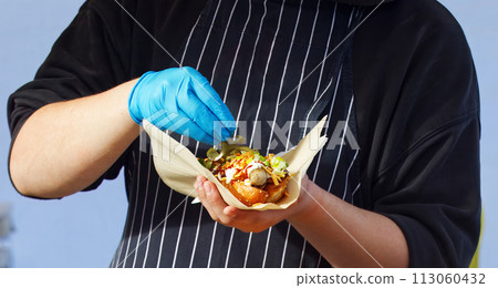 Chef making hot dog for a customer at farmers market. Chef making hot dog for a customer at farmers market. 113060432