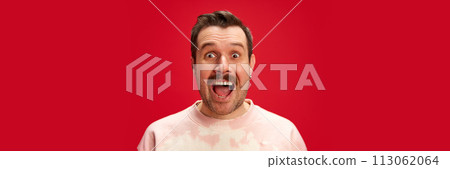 Excited man in tie-dye ping sweatshirt shirt with wide-eyed expression isolated on red studio background. Marketing for unique customer rewards or surprise deals. Excited man in tie-dye ping sweatshirt shirt with wide-eyed expression isolated on red studio background. Marketing for unique customer rewards or surprise deals. 113062064