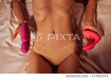 sex vibrator and vacuum stimulator in hands of woman nymphomaniac girl in panties with sexy body lying on a bed. Sex toys for female satisfaction and orgasm 113062355