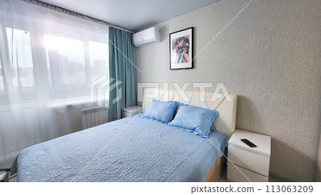 interior of the bedroom with a blue bedspread and pillows on the bed, a bedside table interior of the bedroom with a blue bedspread and pillows on the bed, a bedside table 113063209