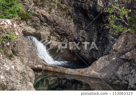 Lively waterfall at Fairy Pools, Isle of Skye, cascades into serene pool, dark rocks embracing Lively waterfall at Fairy Pools, Isle of Skye, cascades into serene pool, dark rocks embracing 113063323