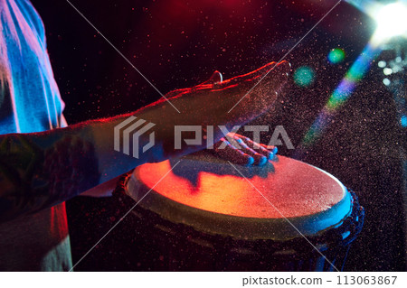 Close-up of male hands, musician playing bongo drums on dark background with stage lights. African culture live event Close-up of male hands, musician playing bongo drums on dark background with stage lights. African culture live event 113063867