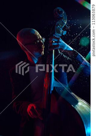 Male musician playing double bass against black background with lights elements. Classical music performance. 113063879