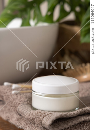 Cosmetic cream jar on beige towels near basin and green monstera in bath, lid mockup Cosmetic cream jar on beige towels near basin and green monstera in bath, lid mockup 113064047