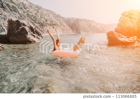 Woman summer sea. Happy woman swimming with inflatable donut on the beach in summer sunny day, surrounded by volcanic mountains. Summer vacation concept. 113066885