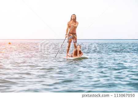 Sea woman and man on sup. Silhouette of happy young woman and man, surfing on SUP board, confident paddling through water surface. Idyllic sunset. Active lifestyle at sea or river. 113067050