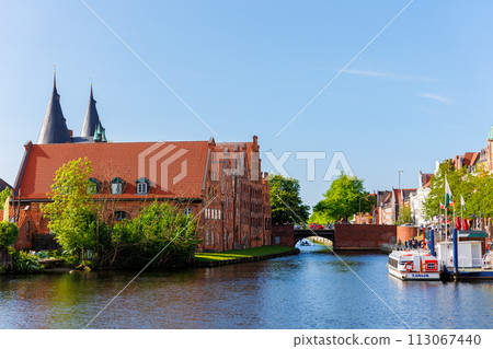 Scenic view panorama Lubeck hanseatic city blue sky sunny summer day. Travemunde Trave river embankment in Lubeck historic Holstentor museum Salzspeicher building in medieval town altstadt Germany 113067440