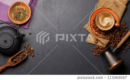 A tantalizing display of roasted coffee beans and dry tea leaves, accompanied by an espresso coffee cup and a teapot 113068087