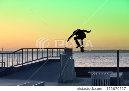 Unrecognizable teenage boy silhouette showing high jump tricks on scooter against 113070537