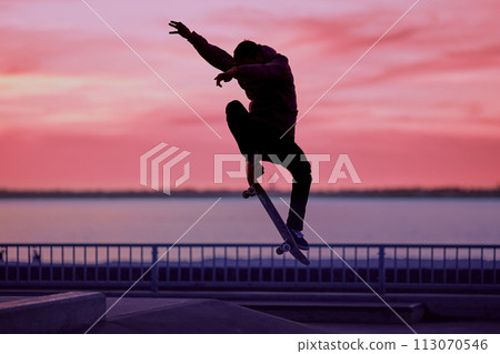 Unrecognizable teenage boy silhouette showing high jump tricks on scooter against 113070546