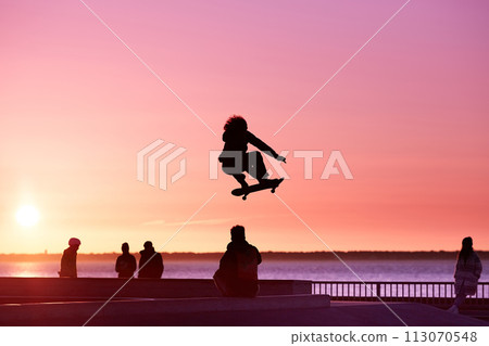 Unrecognizable teenage boy silhouette showing high jump tricks on scooter against Unrecognizable teenage boy silhouette showing high jump tricks on scooter against 113070548