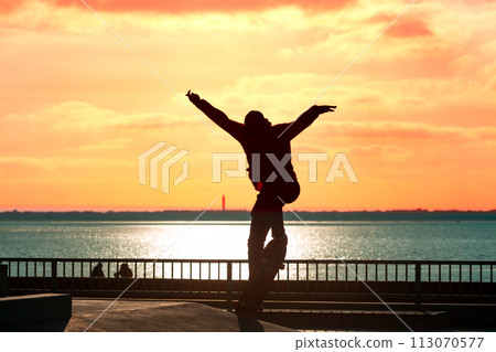 Unrecognizable teenage boy silhouette showing high jump tricks on scooter against Unrecognizable teenage boy silhouette showing high jump tricks on scooter against 113070577