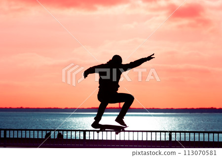 Unrecognizable teenage boy silhouette showing high jump tricks on scooter against 113070581