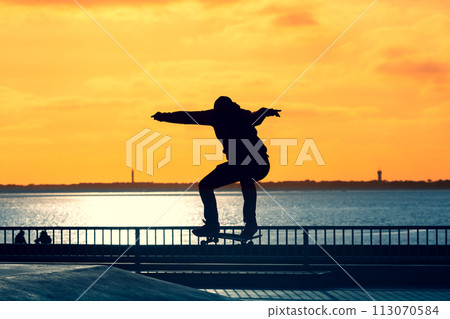 Unrecognizable teenage boy silhouette showing high jump tricks on scooter against Unrecognizable teenage boy silhouette showing high jump tricks on scooter against 113070584