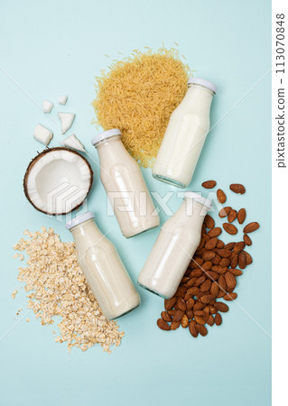 Types of plant-based milk in glass bottles. Coconut, rice, almond and oat milk on blue background. Types of plant-based milk in glass bottles. Coconut, rice, almond and oat milk on blue background. 113070848