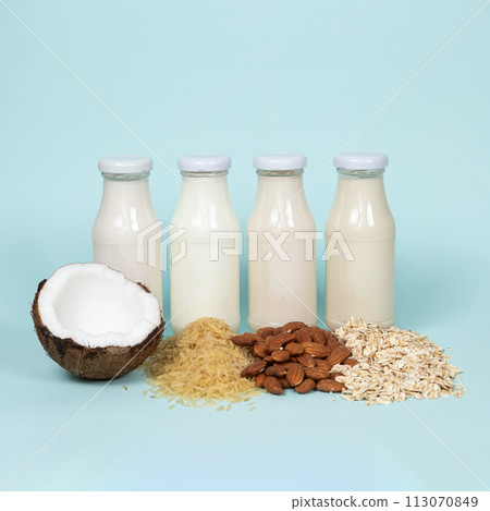 Types of plant-based milk in glass bottles. Coconut, rice, almond and oat milk on blue background. 113070849