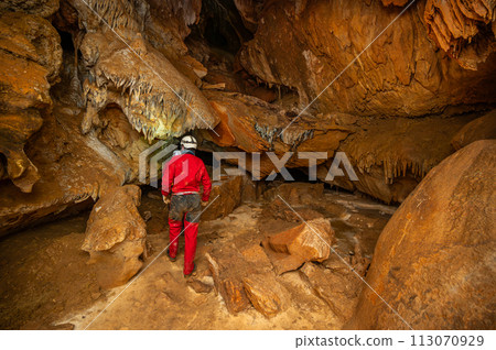 A speleologist with helmet and headlamp exploring a cave with rich stalactite and stalagmite 113070929