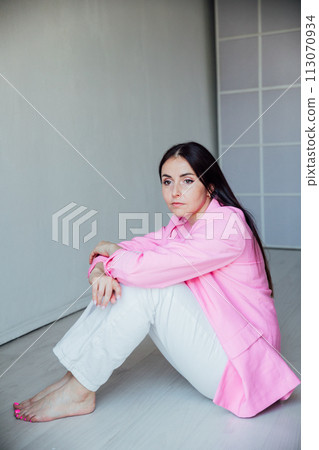 Beautiful fashionable woman sitting on the floor in pink jacket and white pants 113070934